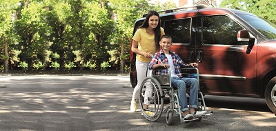 Junge im Rollstuhl mit Auto und Helfer