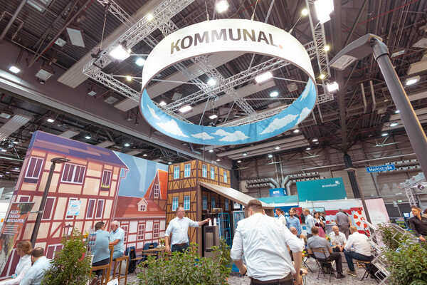 Messestand des Veranstalters mit Messebesuchern. Der Messestand wirkt wie ein typischer Marktplatz