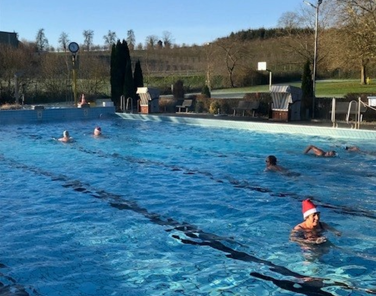Am letzten Tag der Freibadsaison 2024 schwimmen Besucherinnen und Besucher mit Weihnachtsmützen
