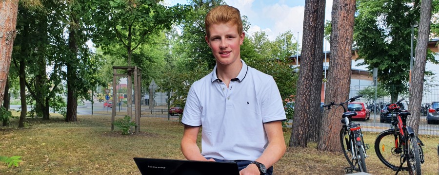 Schüler Sören Twietmeyer mit Laptop auf Bank vor der Schule