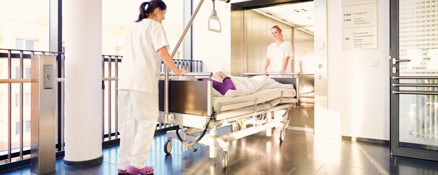 Krankenhaus: Pflegerinnen schieben Patienten im Bett in den Fahrstuhl