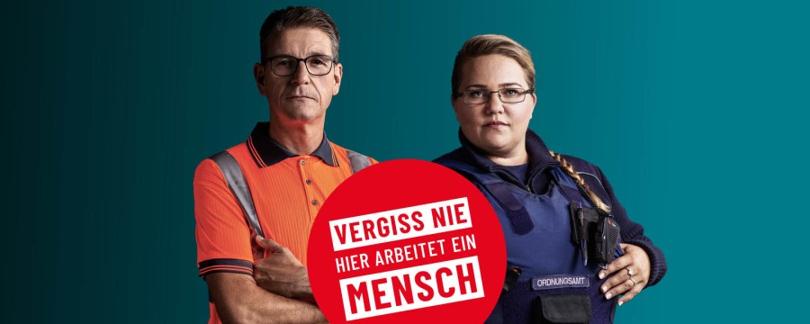 Zwei Personen mit einem Störer auf dem steht: Vergiss nie hier arbeitet ein Mensch