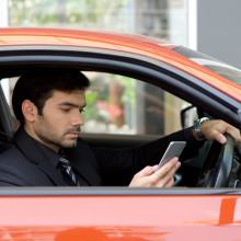 Mann mit Smartphone in rotem Auto.
